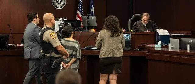 A courtroom with wooden benches and an American flag along with people.